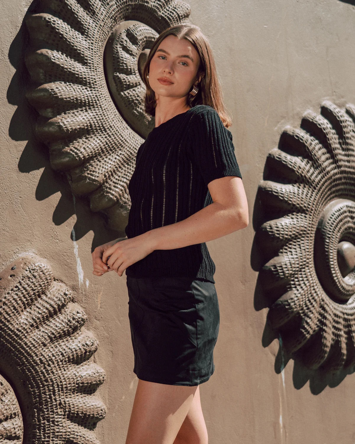 Woman in black outfit standing against a textured wall with decorative elements.