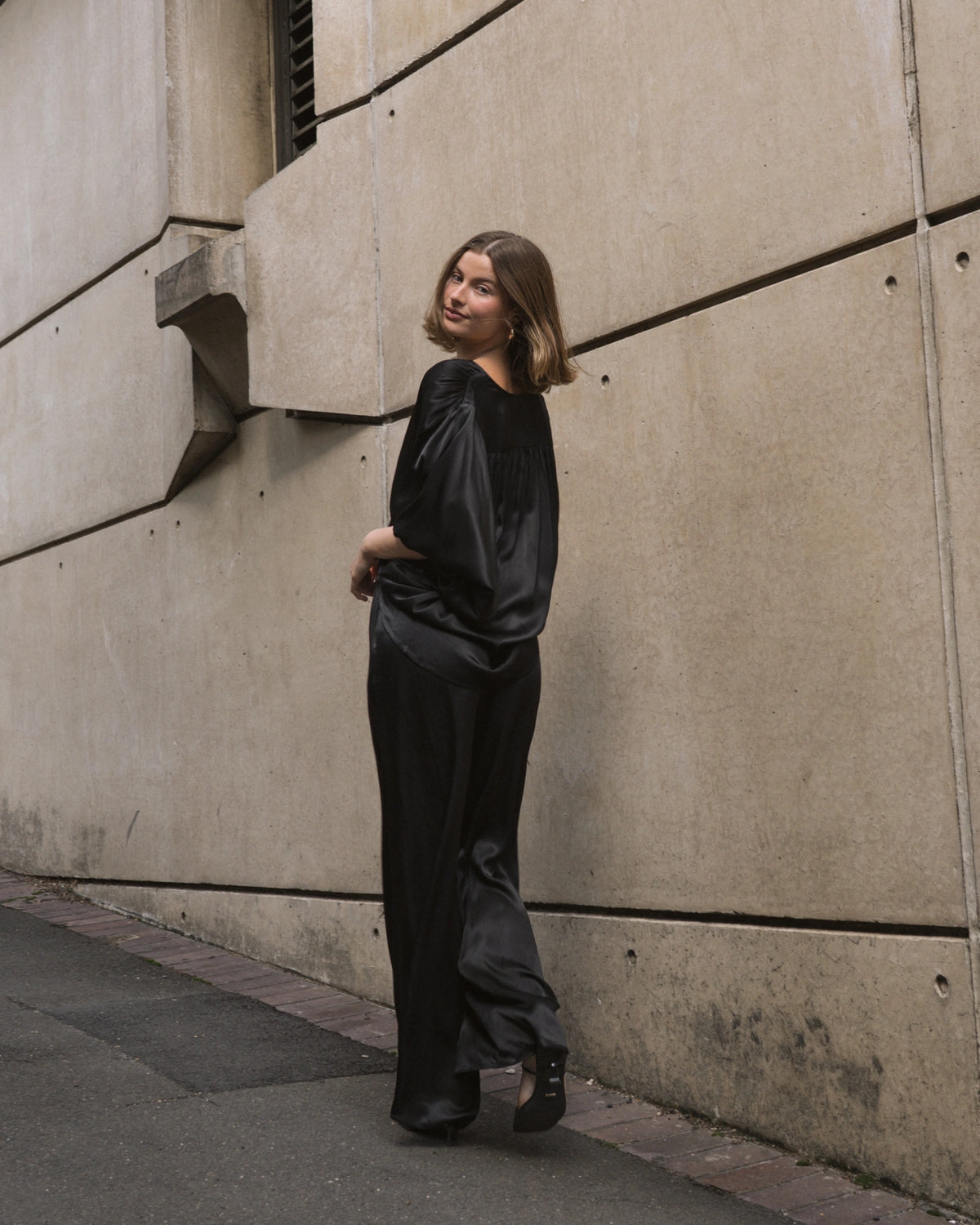Woman in a black outfit standing against a concrete wall.
