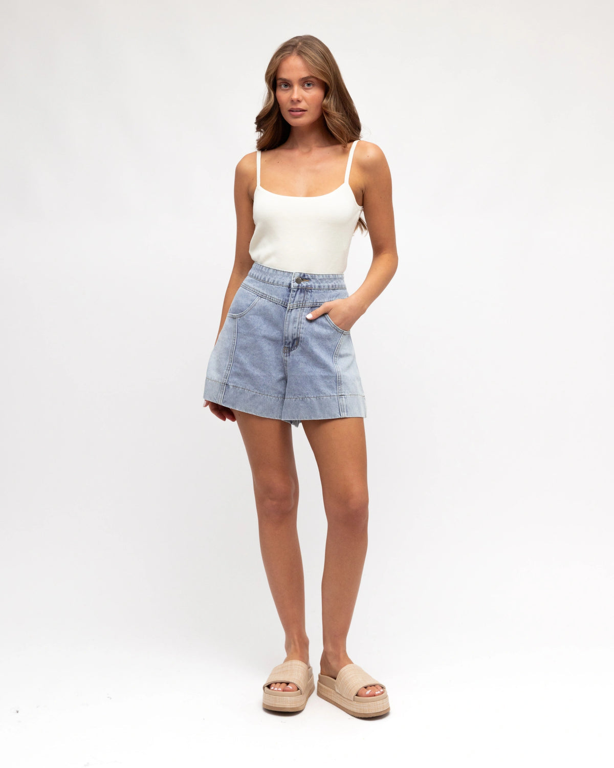Woman wearing a white tank top and light blue denim shorts on a white background