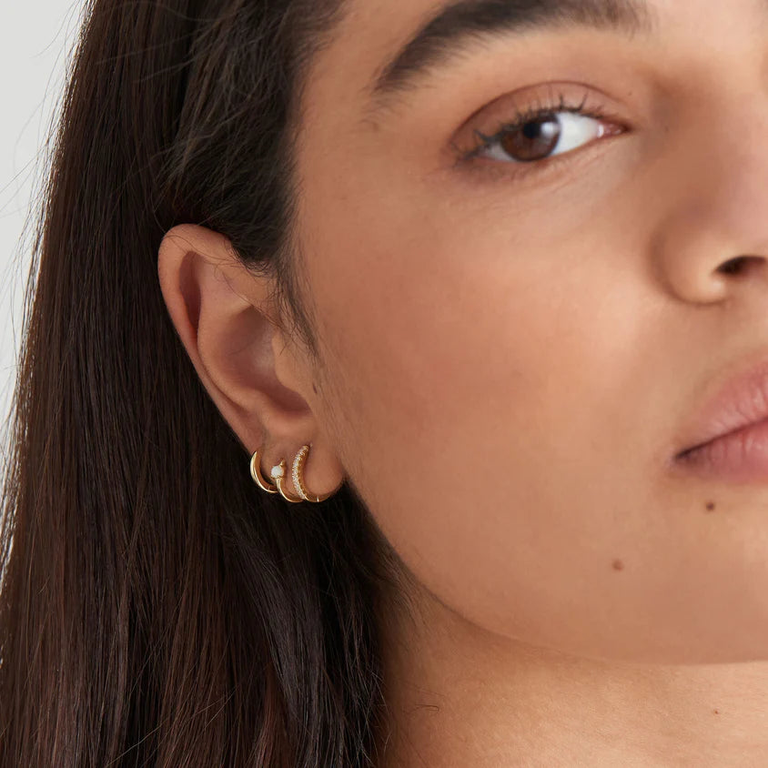 Close-up of a woman wearing gold hoop earrings with a neutral background