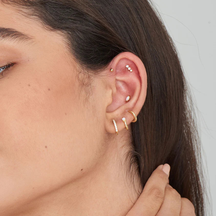 Close-up of an ear with gold hoop earrings against a neutral background