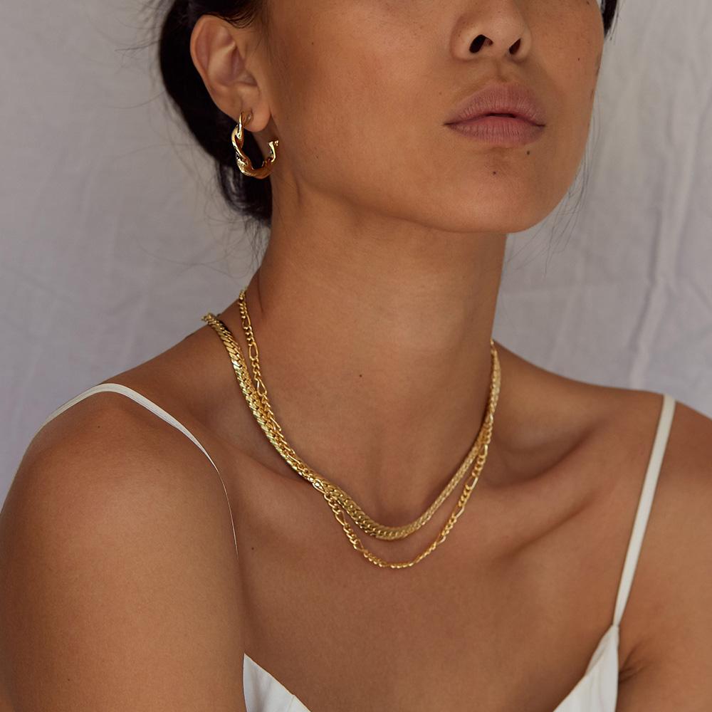 Woman wearing a gold necklace and hoop earrings against a neutral background
