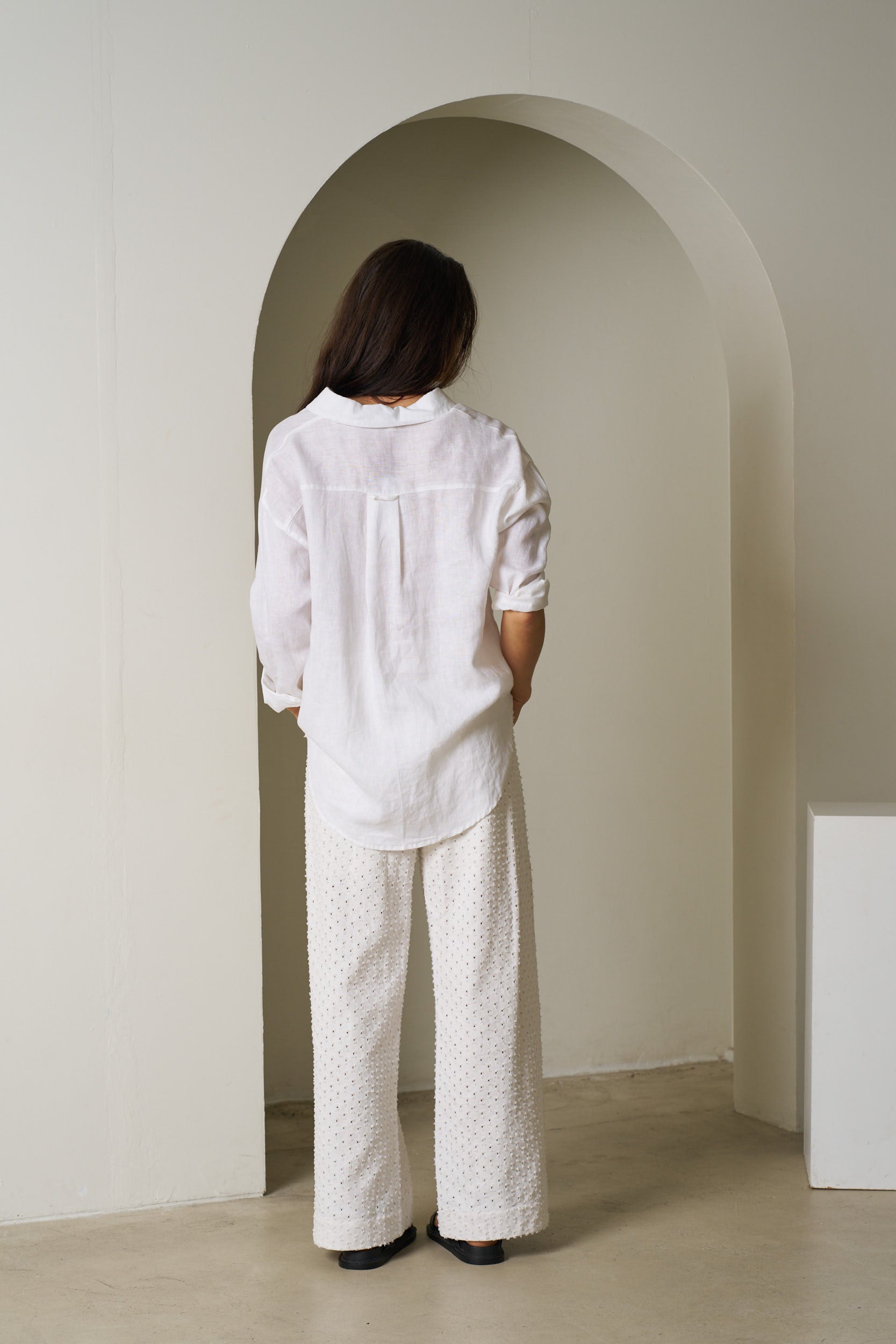 Person wearing a white outfit standing in an archway with a neutral background